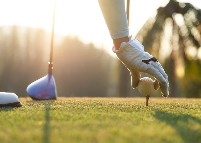 hand of woman golf player gentle put a golf ball onto wooden tee on the tee off, to make ready hit away from tee off to the fairway ahead. Healthy and Lifestyle Concept. hand of woman golf player gentle put a golf ball onto wooden tee on the tee off, to make ready hit away from tee off to the fairway ahead. Healthy and Lifestyle Concept.